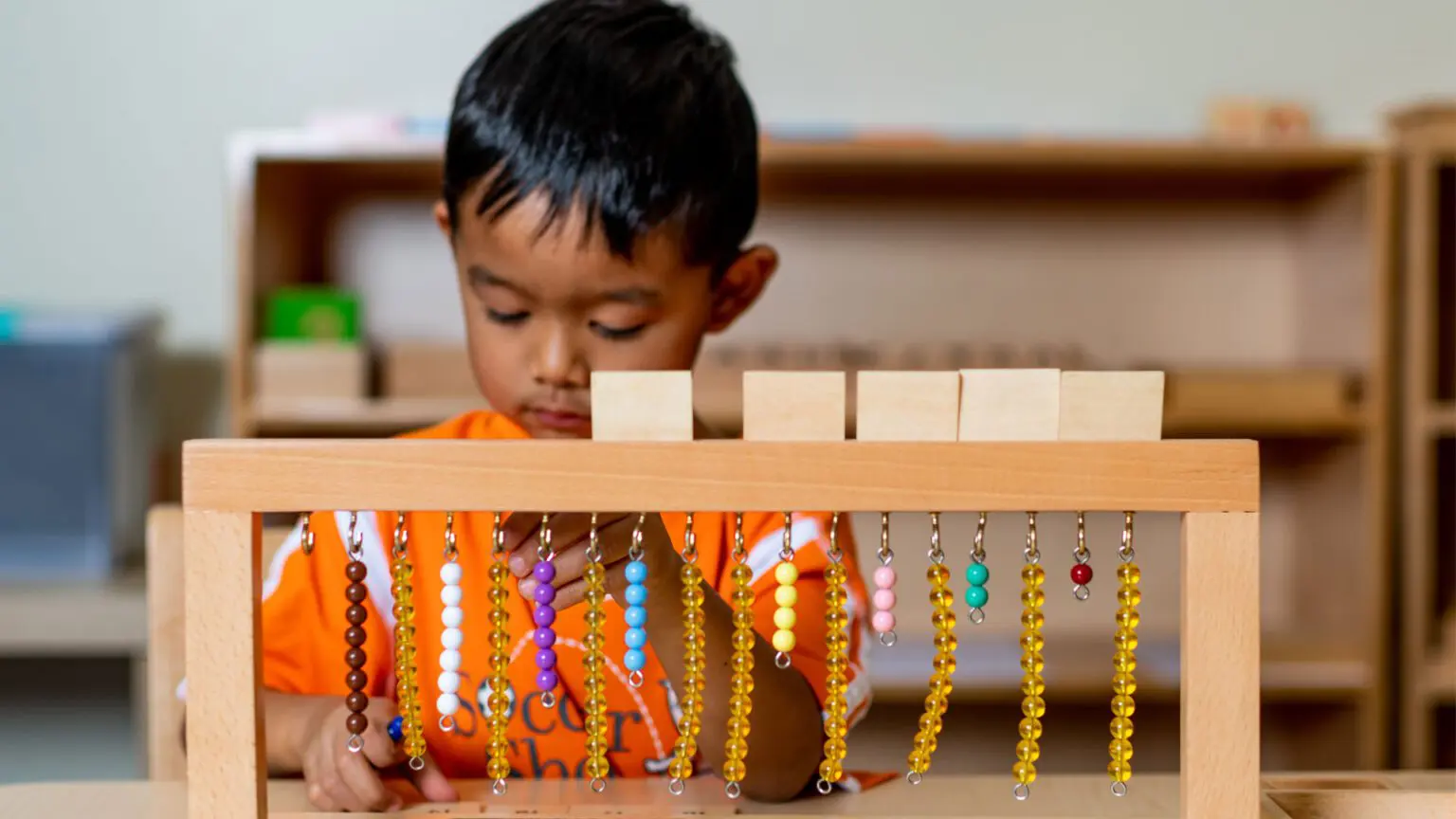 A boy is playing with beads on the table.