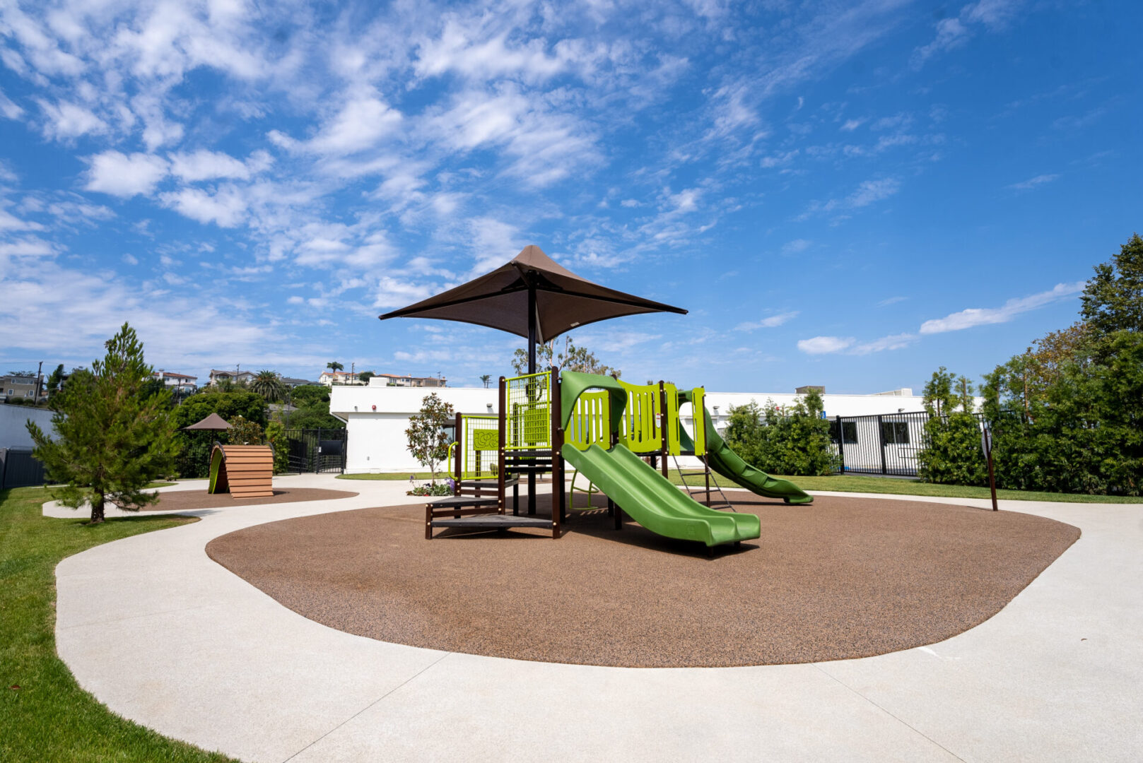 A playground with a green slide and umbrella.